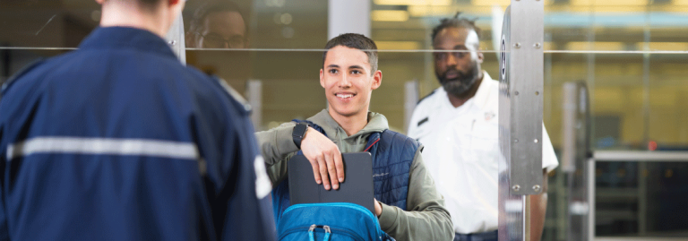 Traveller at security screening checkpoint removing their black laptop from a blue backpack.