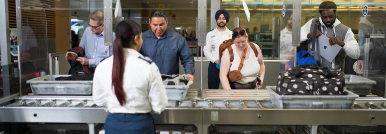 Un groupe de personnes retirent leurs effets personnels sous le regard d'agents de contrôle.