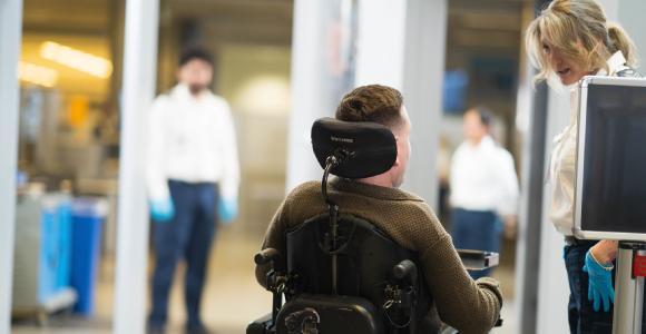 A male passenger in a wheelchair with a service dog speaking with a female screening officer. 
