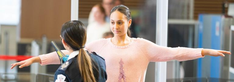 A screening officer is using a hand held metal detector on a young passenger. 