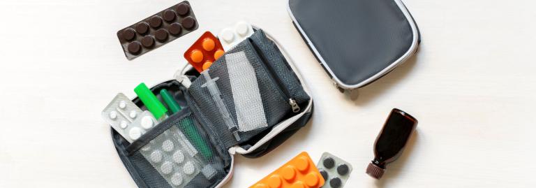 Pochette de voyage ouverte contenant divers sachets de pilules et des flacons de médicaments disposés sur une surface blanche. 