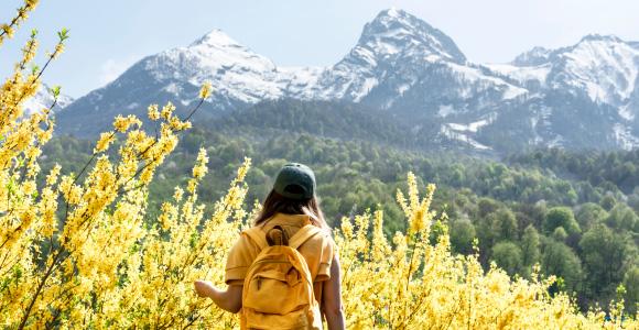 A hiker surrounded by spring flowers looks out towards a mountain range. 