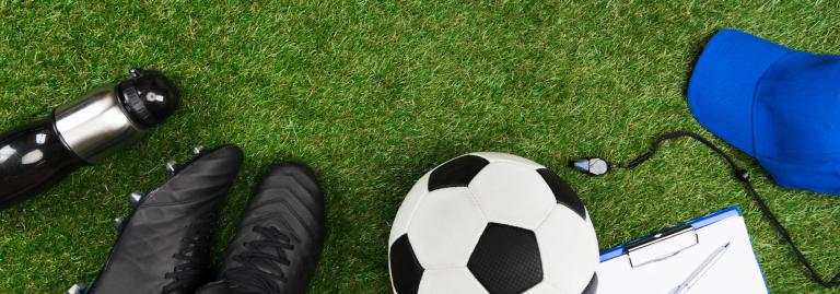 Soccer ball, cleats, whistle, hat and water bottle laying on grass