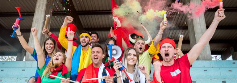 Un groupe de jeunes adultes qui encouragent lors d’un événement sportif. Ils ont des trompettes à air, des drapeaux et du confetti qui éclate.