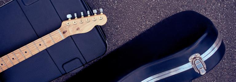Une valise, une guitare et un étui à guitare reposent sur la chaussée.
