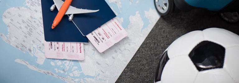 Carte géographique posée à plat, sur laquelle est placée une valise, un ballon de soccer, des passeports, des cartes d’embarquement et un petit avion jouet.