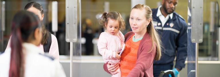 Une passagère tenant un enfant en bas âge parle à une agente de contrôle à la zone de retrait des effets personnels.