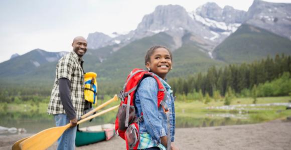 Un adulte et un enfant portant de l’équipement de canotage sourient. On voit un lac et des montagnes en arrière-plan.