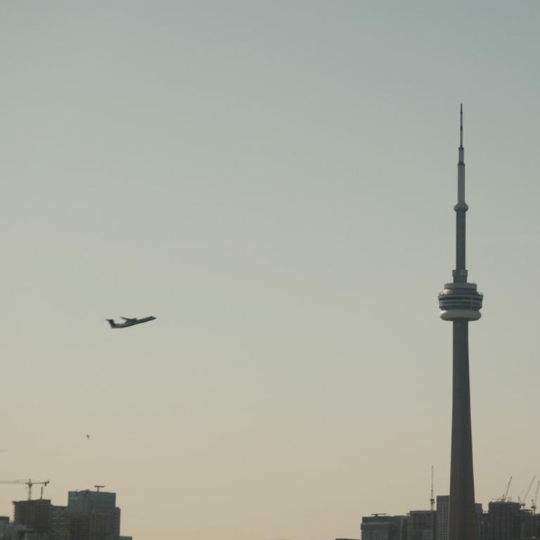 Avion survolant la Tour CN de Toronto, au-dessus de la ligne d'horizon de la ville.