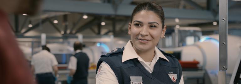 A female screening officer is smiling while scanning an electronic boarding pass. 