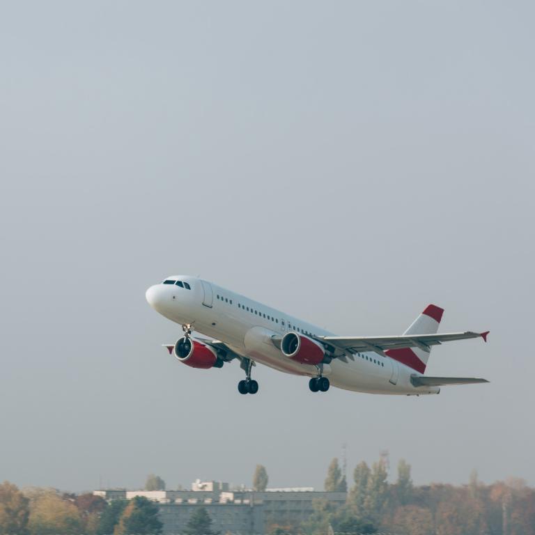 Un avion blanc et rouge s’élève dans un ciel gris au-dessus d’une ville.